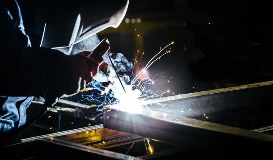 A close up of someone in a welding mask welding with a bright spark.